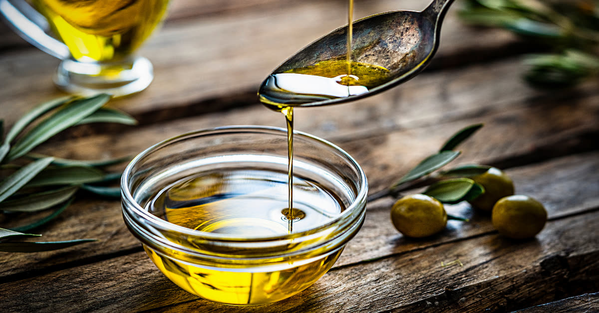 Natives Olivenoel extra wird von einem Loeffel in eine Glasschale gegossen